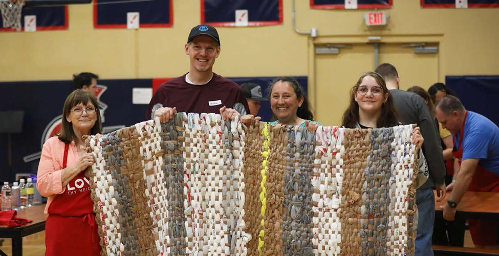 Four individuals standing in front of a woven mat smiling at camera