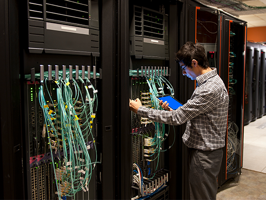 Photo of male standing next to tall server with blue and green cables