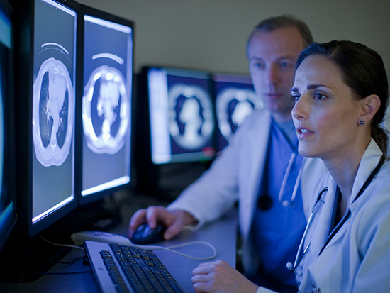 Woman and man sitting in front of computer monitors looking at brain scan