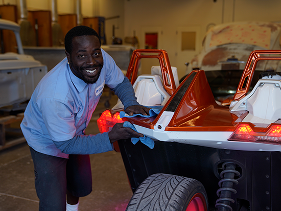 Photo of male student in blue shirt wiping the exterior of an orange car.