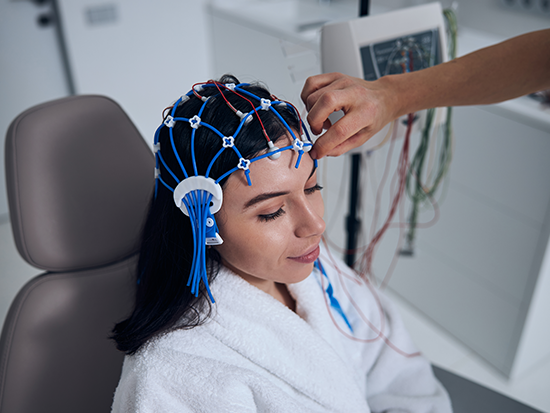 Woman with blue cables on her hair, wearing a white robe, sitting in tan chair