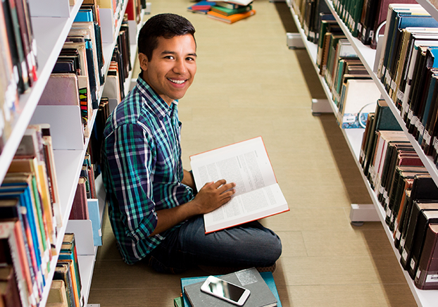 Student sitting on floor with a pile of books 