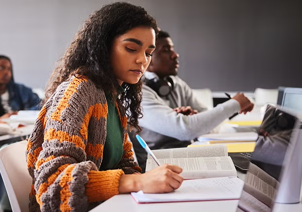 Female student wearing a chunky cardigan writing notes in a classroom