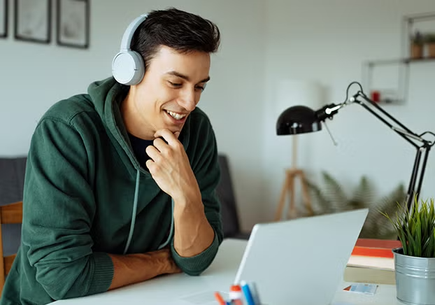 Male student wearing headphones looking eagerly at a laptop