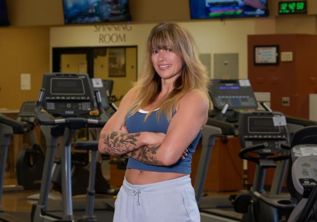 Woman wearing a grey tank top and sweat pants standing in from of treadmill in the gym.