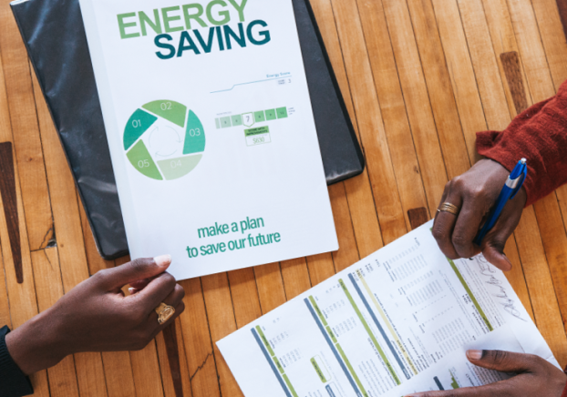 Image of wooden table with documents that say "Energy Saving" with two hand on the table